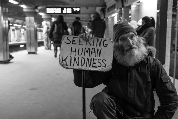 Image of homeless gentleman holding a sign that reads "Seeking Human Kindness."