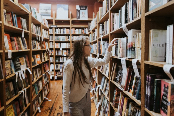 A young woman examines books on a shelf.