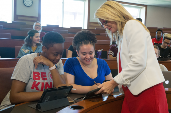 Instructor holding iPad speaks with two students 