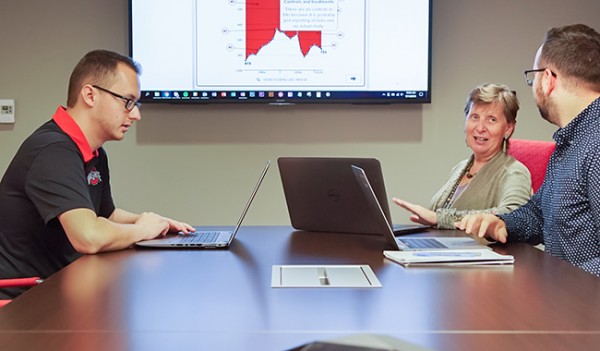 Instructional design staff meet with a faculty member to review a sample figure on a large television screen.