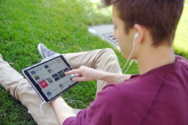 Student sitting on the grass looking at and selecting a podcast on his ipad