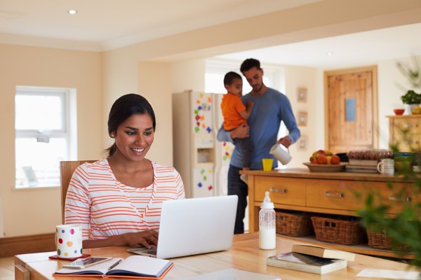 A woman working on a laptop while her child and husband look on.