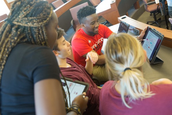 Students work together in a classroom gathered around a central iPad 