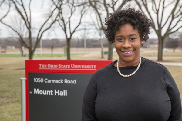 Photo of a smiling woman standing outside in front of the Mount Hall sign.