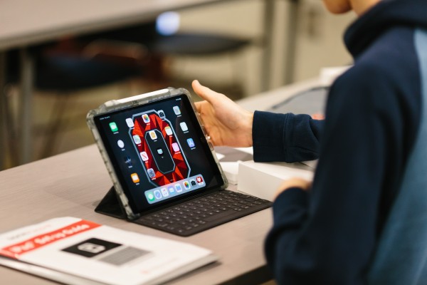 Student holding iPad displays Block O wallpaper in red on grey backdrop