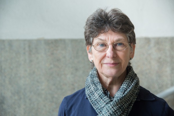 A woman with short grey hair wearing a scarf looks straight ahead