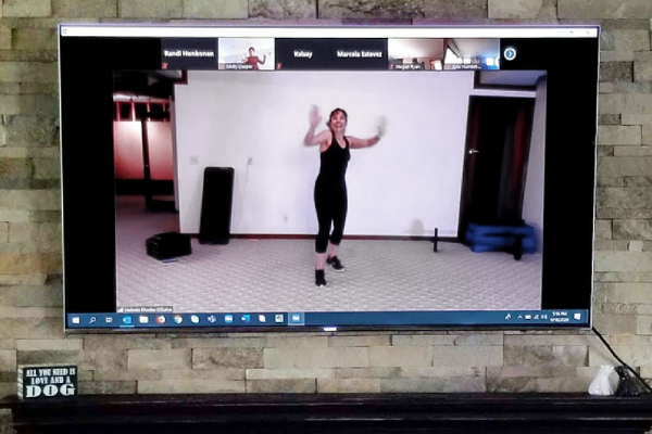 Melinda Rhodes-DiSalvo demonstrating a Zumba move on a television via zoom