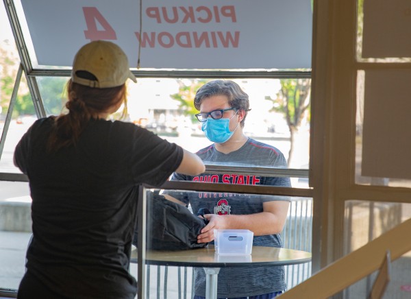 A Digital Flagship staff member passes a backpack containing an iPad kit out of a window to an Ohio State student.