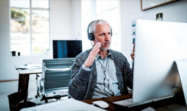 Man with headset gesturing at computer screen