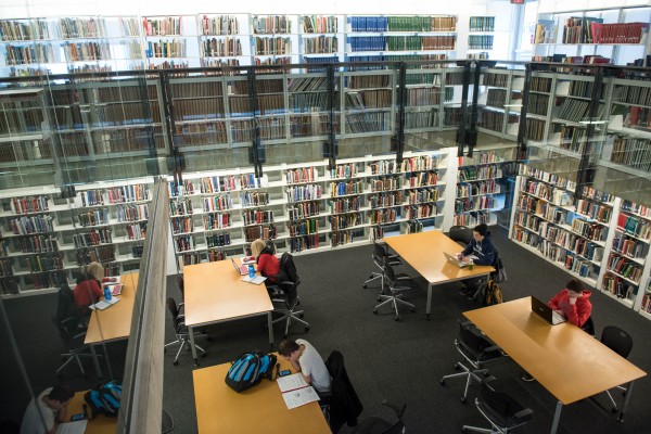 Four students study at separate tables amid the stacks in Thompson Library