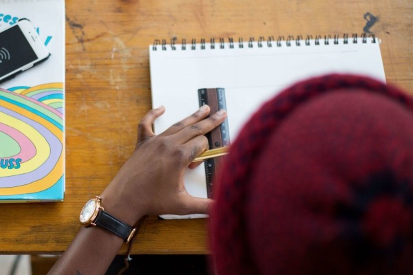 A person lines up a ruler on a drawing notebook, pencil ready to begin sketching