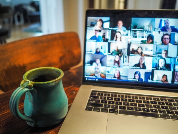 A mug sits next to a laptop, the screen showing a large virtual gathering on Zoom