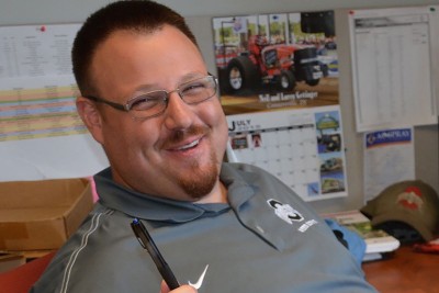 Bruce Ackley sits at a desk, smiling and wearing an Ohio State polo shirt